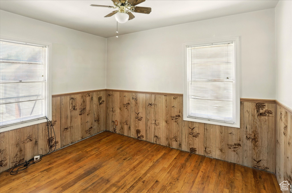 Spare room featuring a wainscoted wall, ceiling fan, wood walls, and wood finished floors