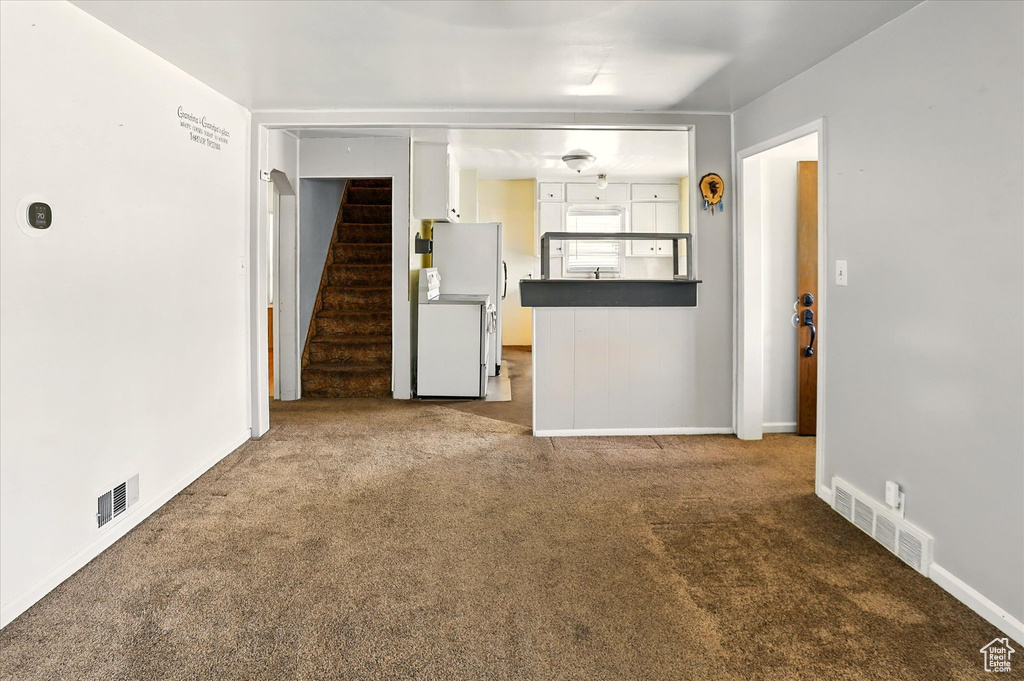 Unfurnished living room with carpet floors, stairway, and baseboards