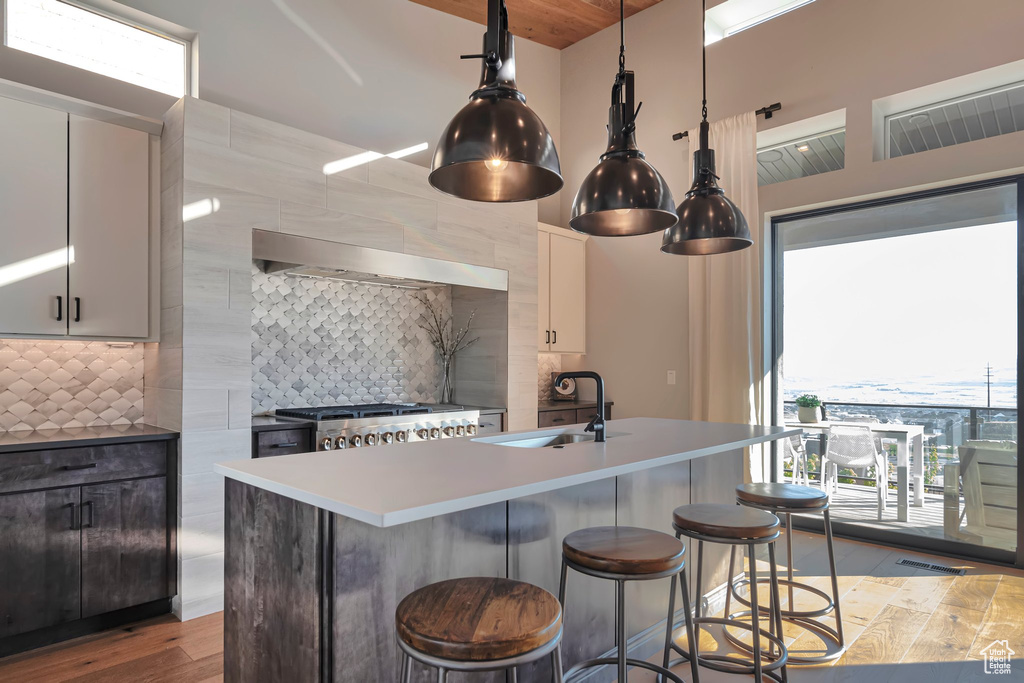 Kitchen featuring decorative backsplash, wood finished floors, a kitchen bar, an island with sink, and light countertops