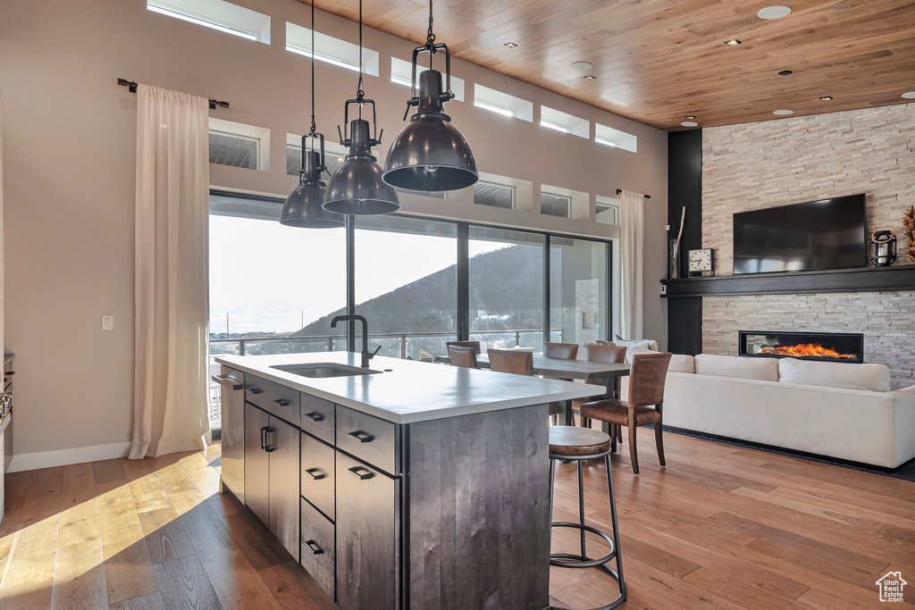 Kitchen with a towering ceiling, wood ceiling, light wood-style flooring, a center island with sink, and a stone fireplace