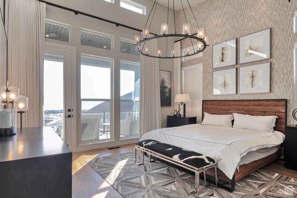 Bedroom with a chandelier, access to exterior, wood finished floors, and a high ceiling