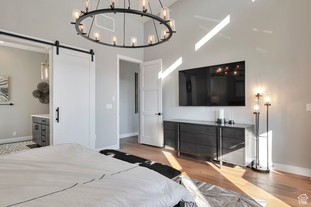 Bedroom featuring a barn door, wood finished floors, a towering ceiling, and a chandelier