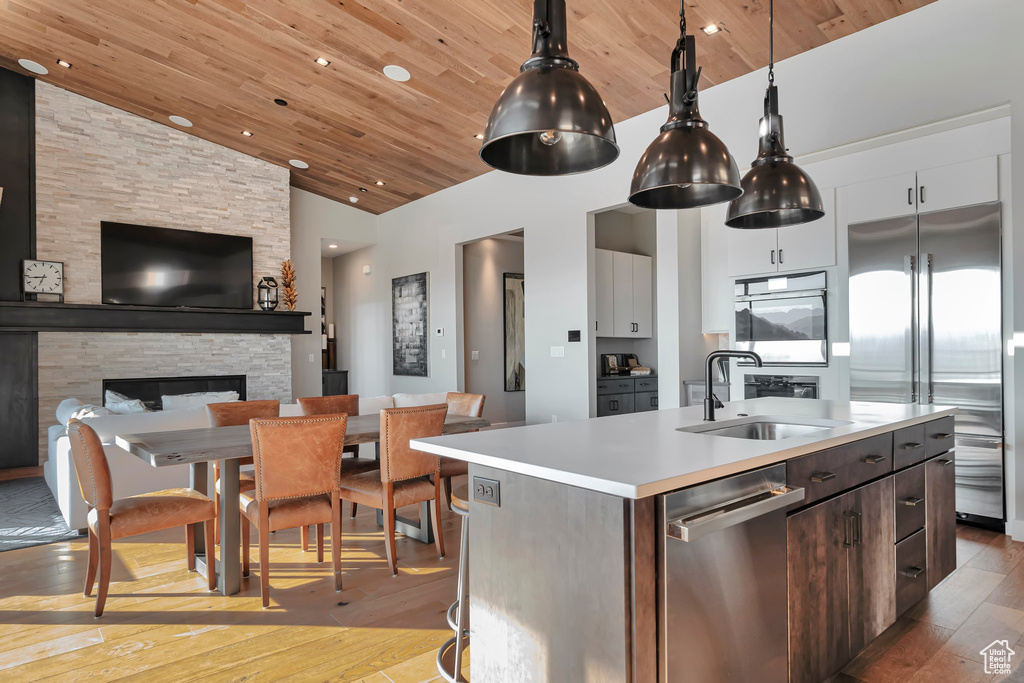 Kitchen featuring stainless steel appliances, light wood-type flooring, light countertops, an island with sink, and wooden ceiling