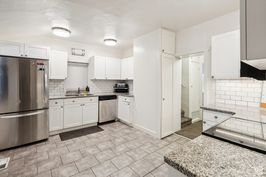 Kitchen featuring appliances with stainless steel finishes, decorative backsplash, white cabinets, and light stone counters