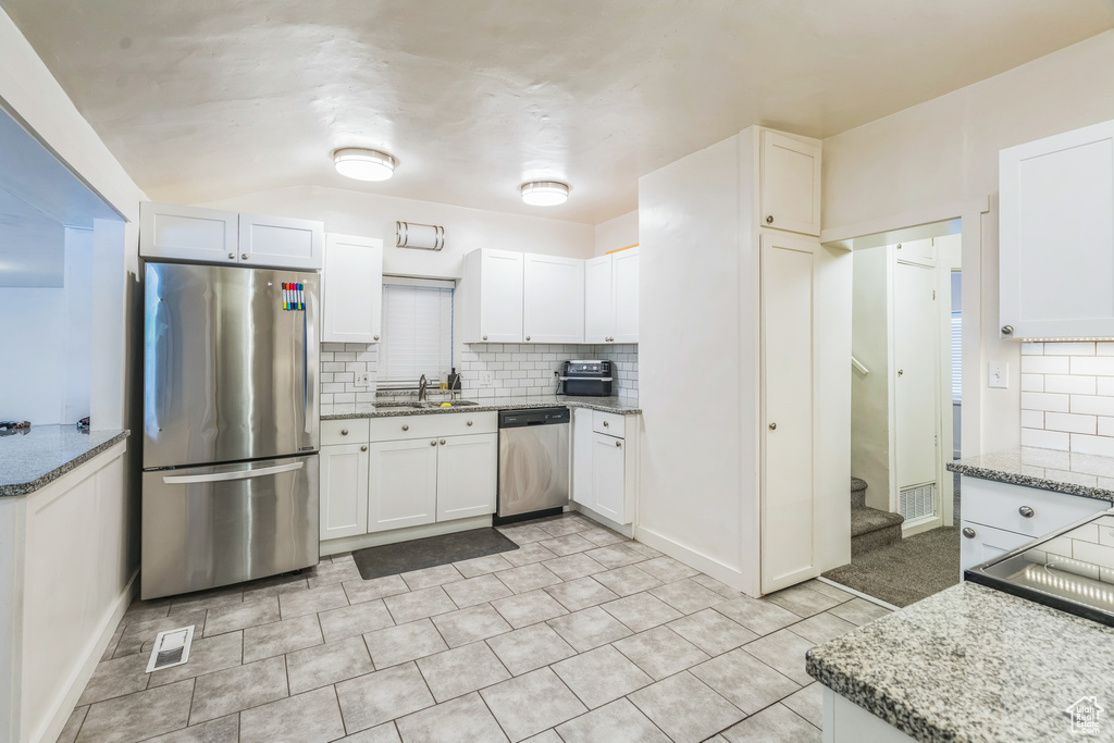 Kitchen with appliances with stainless steel finishes, tasteful backsplash, light stone counters, and white cabinets