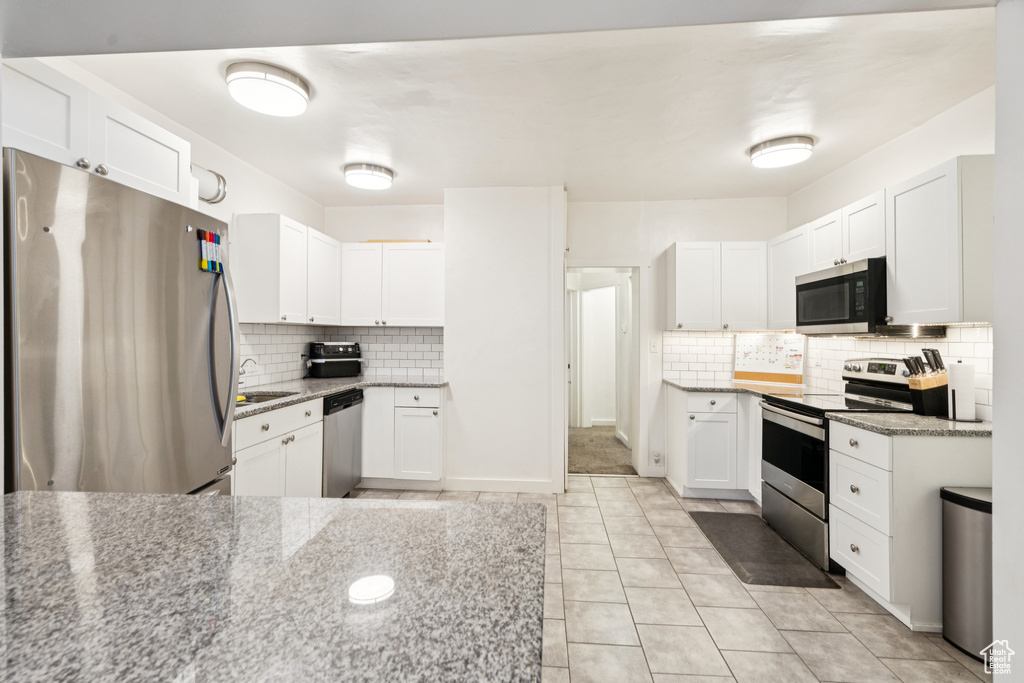 Kitchen with stainless steel appliances, decorative backsplash, and white cabinetry