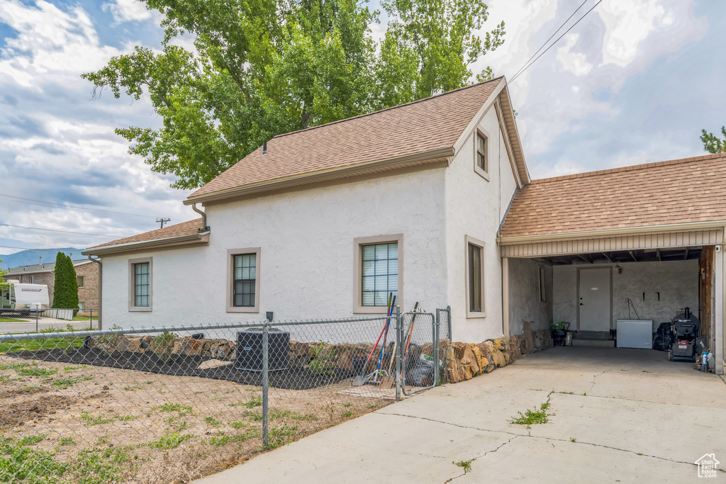 View of side of home with stucco siding, concrete driveway, a shingled roof, and a carport