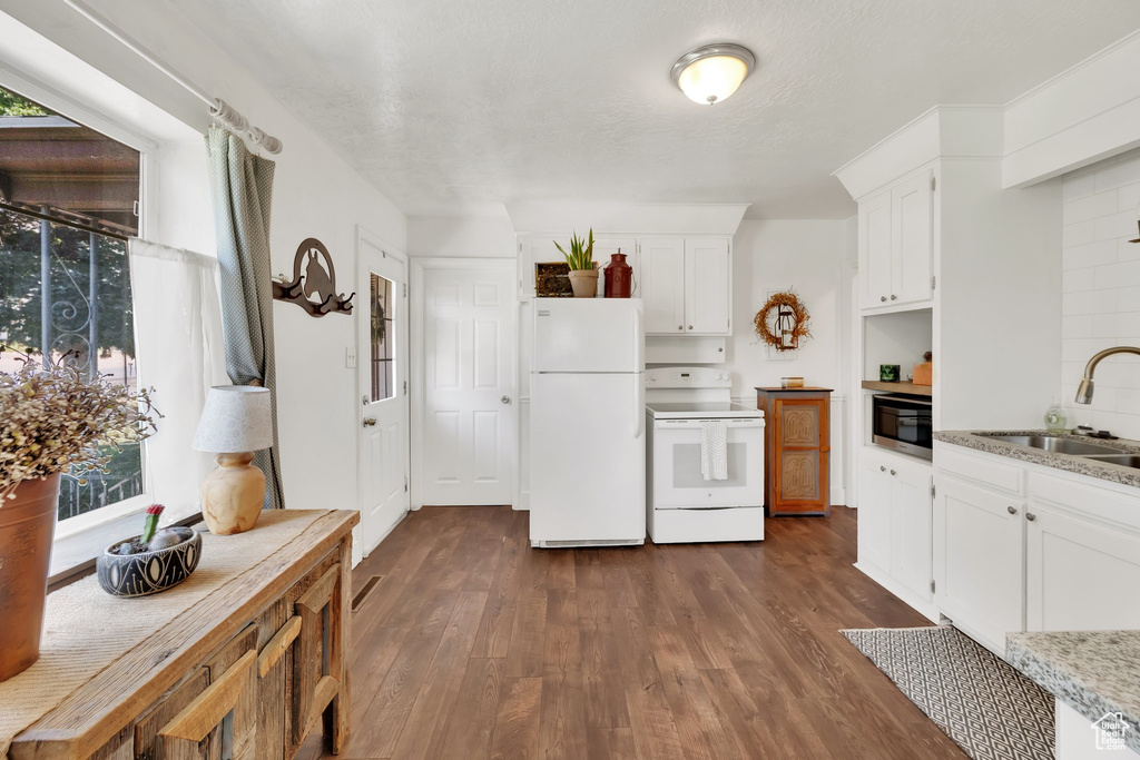 Kitchen featuring white appliances, dark wood-type flooring, white cabinets, and plenty of natural light