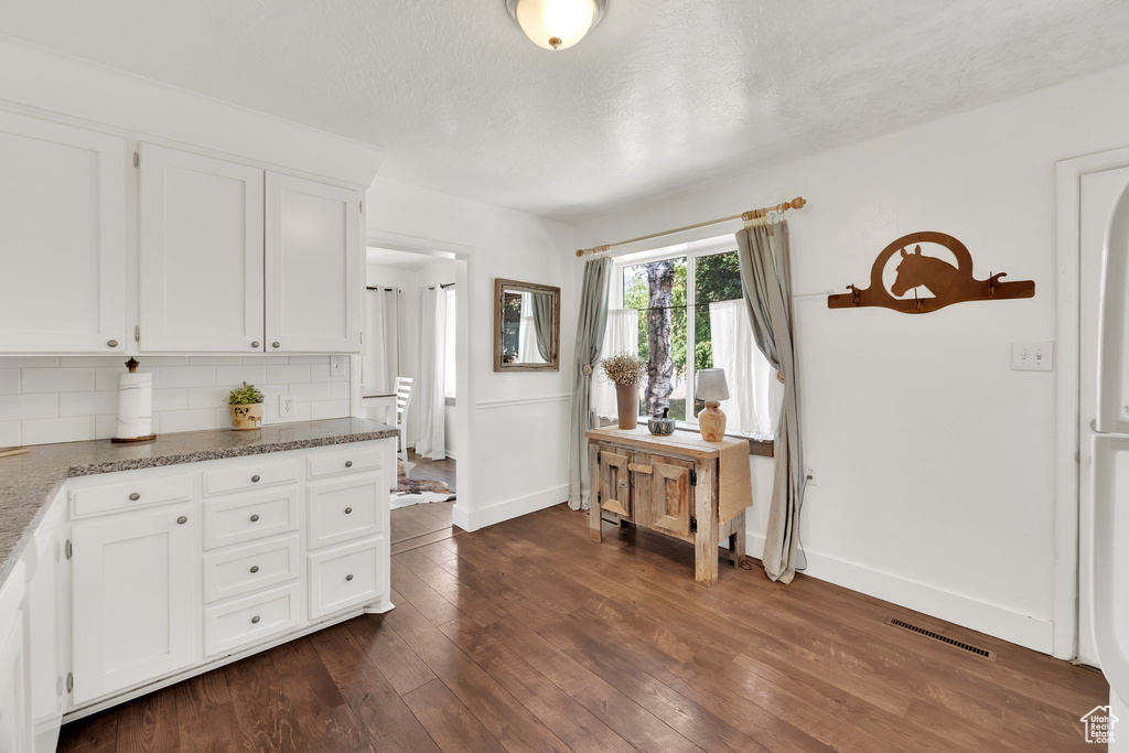 Kitchen with white cabinets, tasteful backsplash, dark wood finished floors, light stone countertops, and a textured ceiling