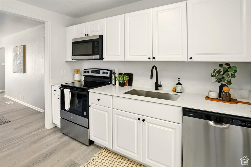 Kitchen featuring stainless steel appliances, light wood-style floors, light countertops, and white cabinets