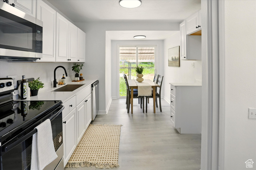Kitchen featuring stainless steel appliances, light wood-type flooring, light countertops, and white cabinetry