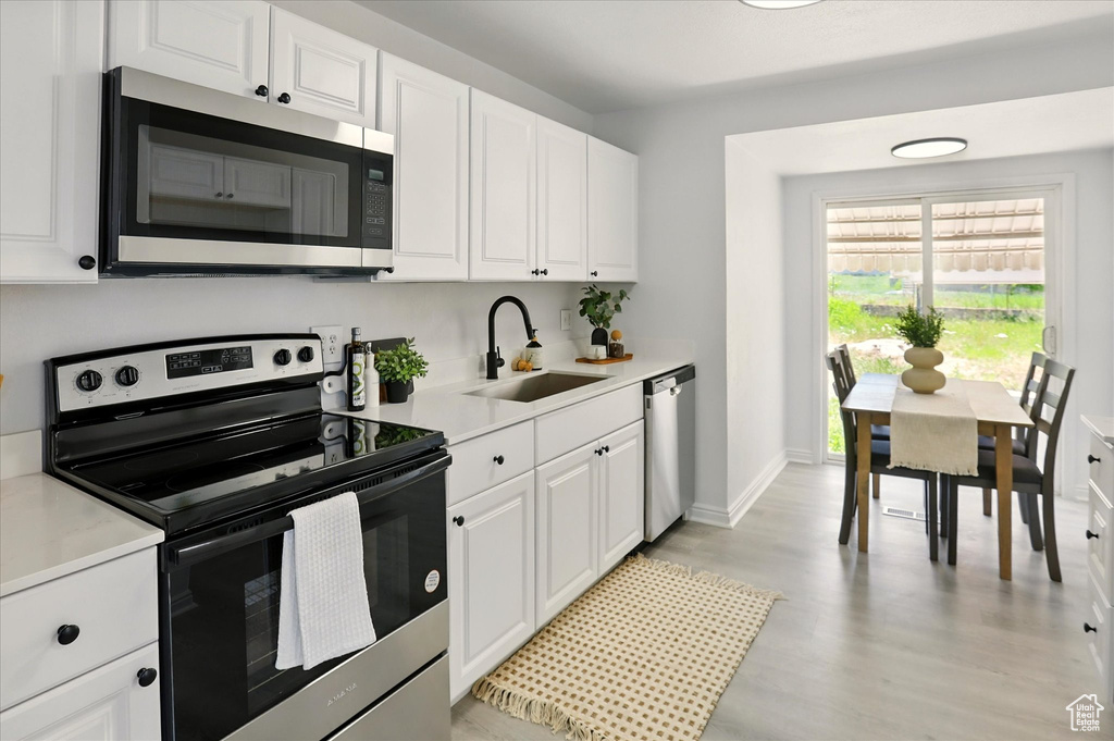 Kitchen with stainless steel appliances, white cabinetry, light wood-style floors, and light countertops