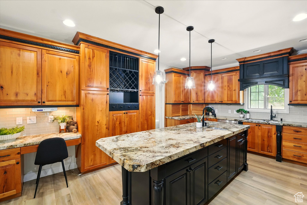 Kitchen featuring tasteful backsplash, light wood-style floors, brown cabinetry, built in study area, and recessed lighting