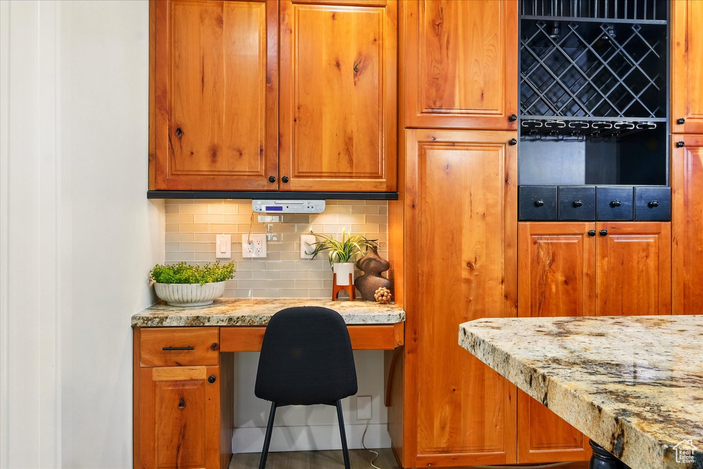 Kitchen featuring backsplash, built in study area, light stone countertops, and brown cabinets