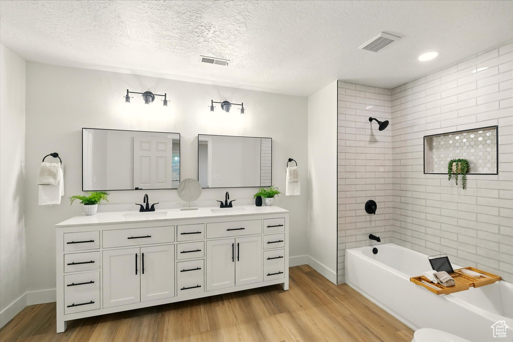 Full bathroom with wood finished floors, double vanity, washtub / shower combination, and a textured ceiling