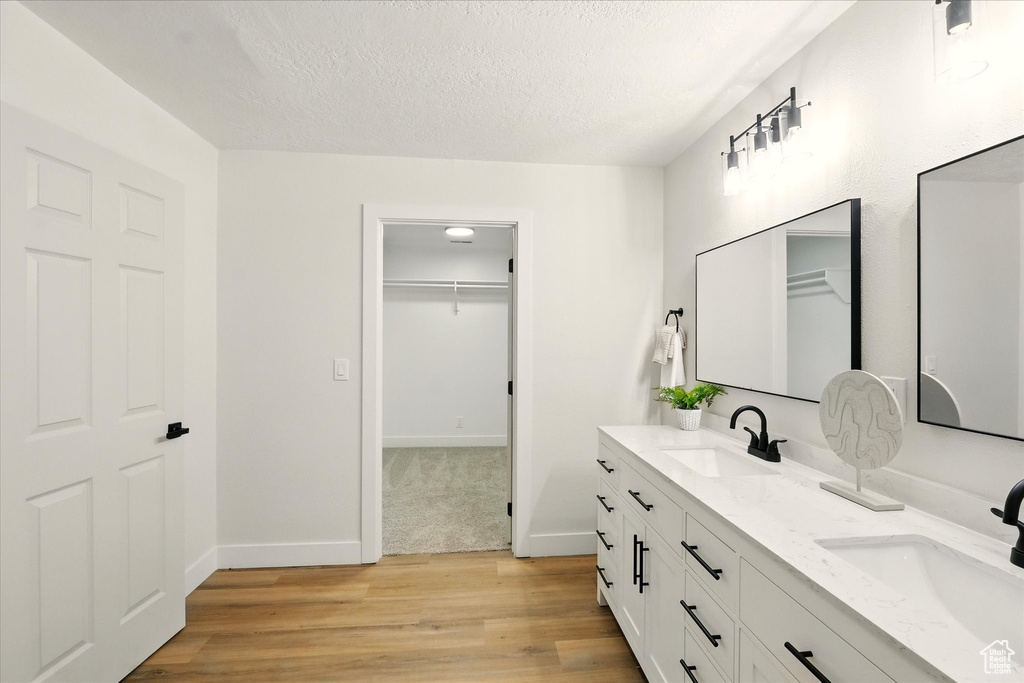 Full bath featuring double vanity, wood finished floors, a textured ceiling, and a walk in closet