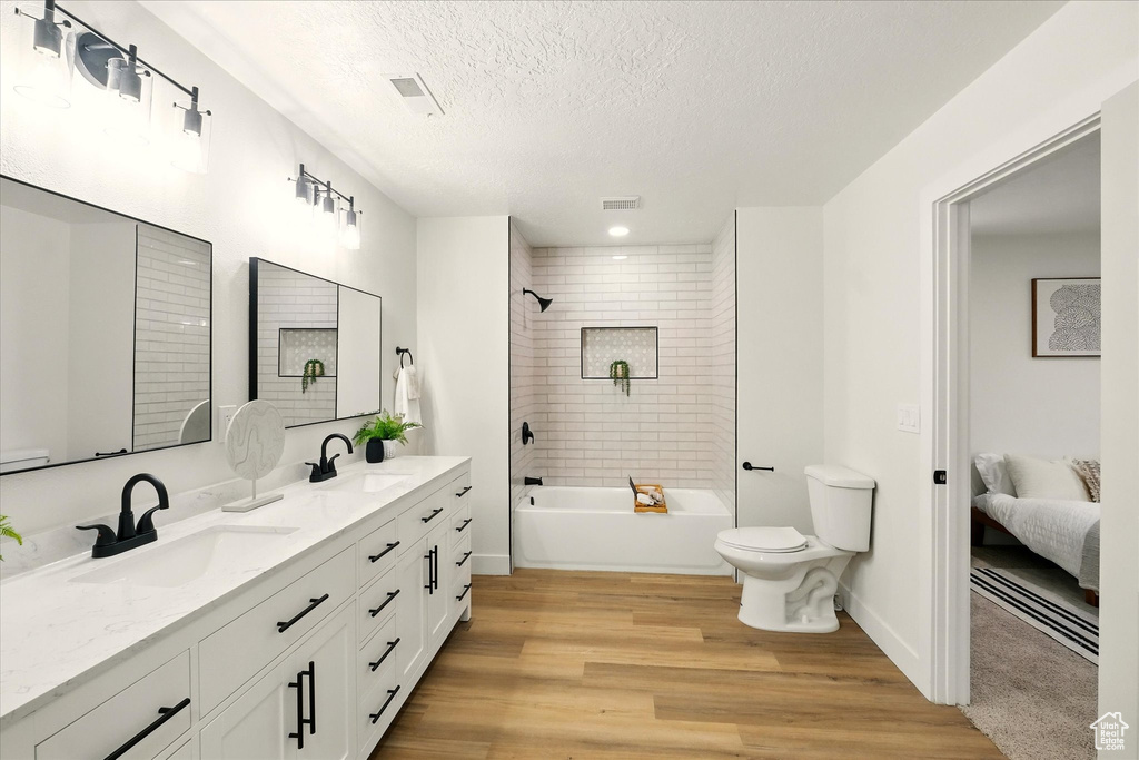 Ensuite bathroom with wood finished floors, double vanity, a textured ceiling, and bathing tub / shower combination