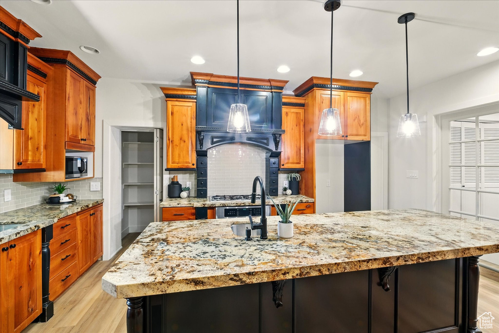 Kitchen with light wood-type flooring, backsplash, a kitchen island with sink, light stone countertops, and recessed lighting