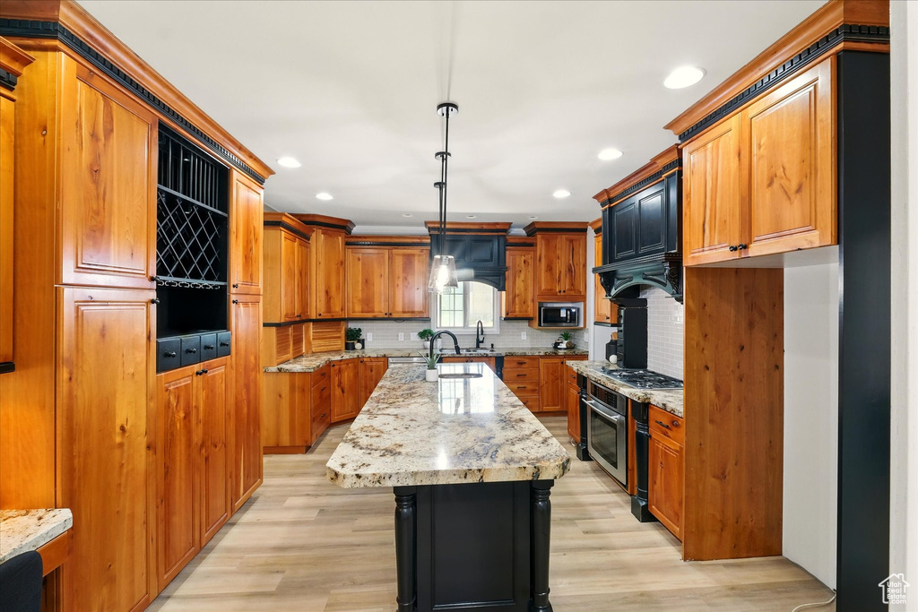 Kitchen with appliances with stainless steel finishes, a center island with sink, brown cabinetry, light wood-type flooring, and recessed lighting