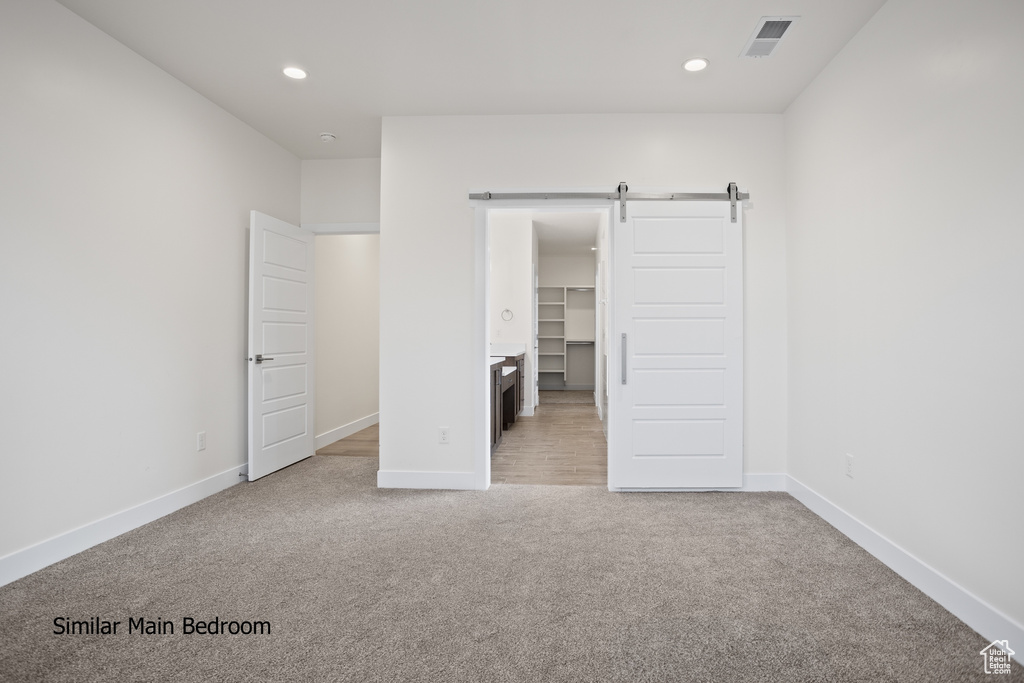 Unfurnished bedroom featuring carpet, a barn door, a spacious closet, and recessed lighting