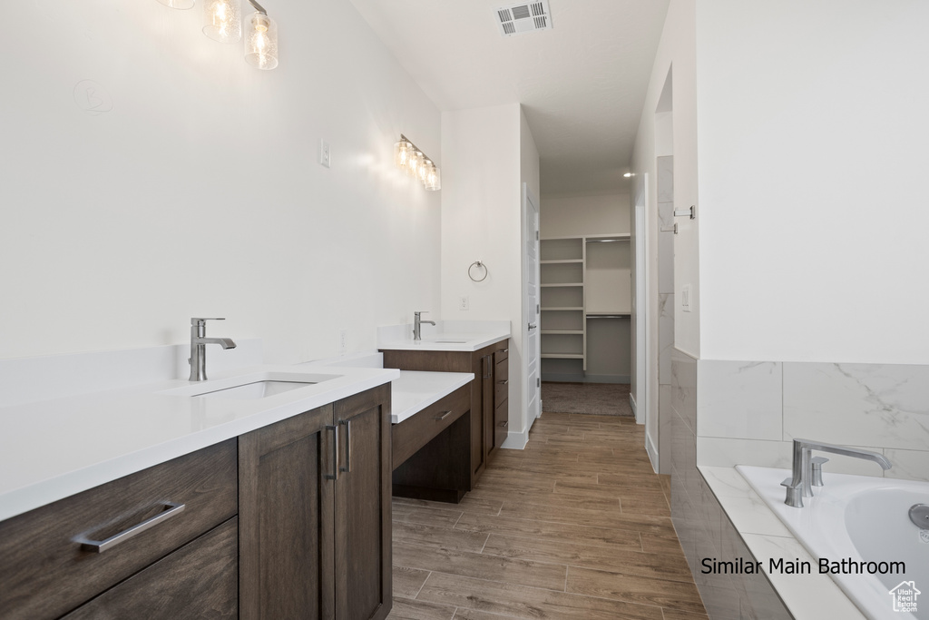 Full bathroom featuring two vanities, a bath, a walk in closet, and wood finished floors