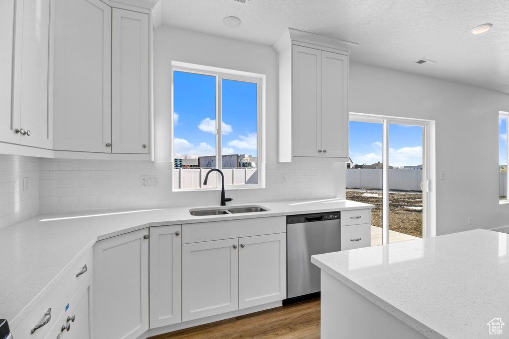 Kitchen with dishwasher, backsplash, wood finished floors, white cabinets, and light stone counters