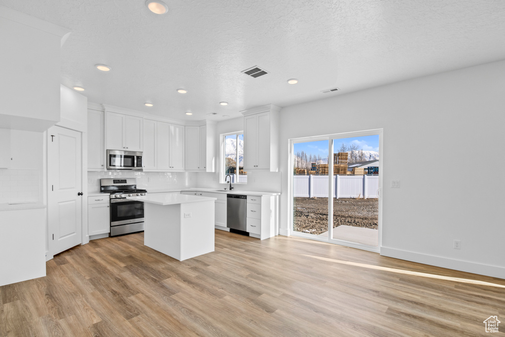 Kitchen with stainless steel appliances, light wood-style flooring, recessed lighting, white cabinetry, and a center island