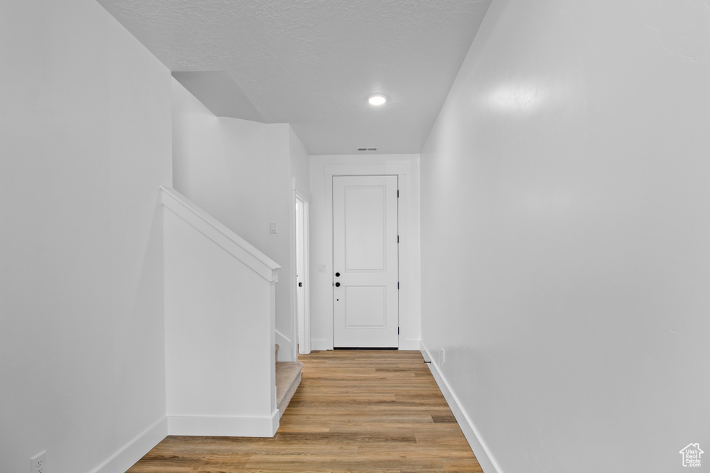 Corridor featuring stairs, light wood-type flooring, a textured ceiling, and recessed lighting