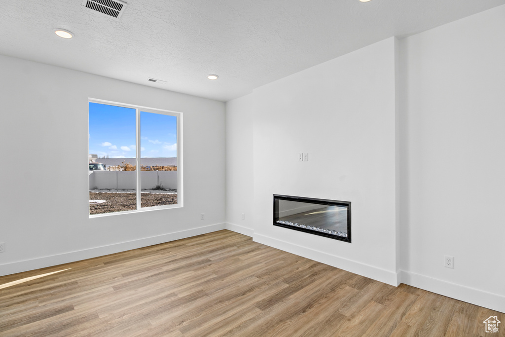 Unfurnished living room featuring wood finished floors, a glass covered fireplace, recessed lighting, and a textured ceiling