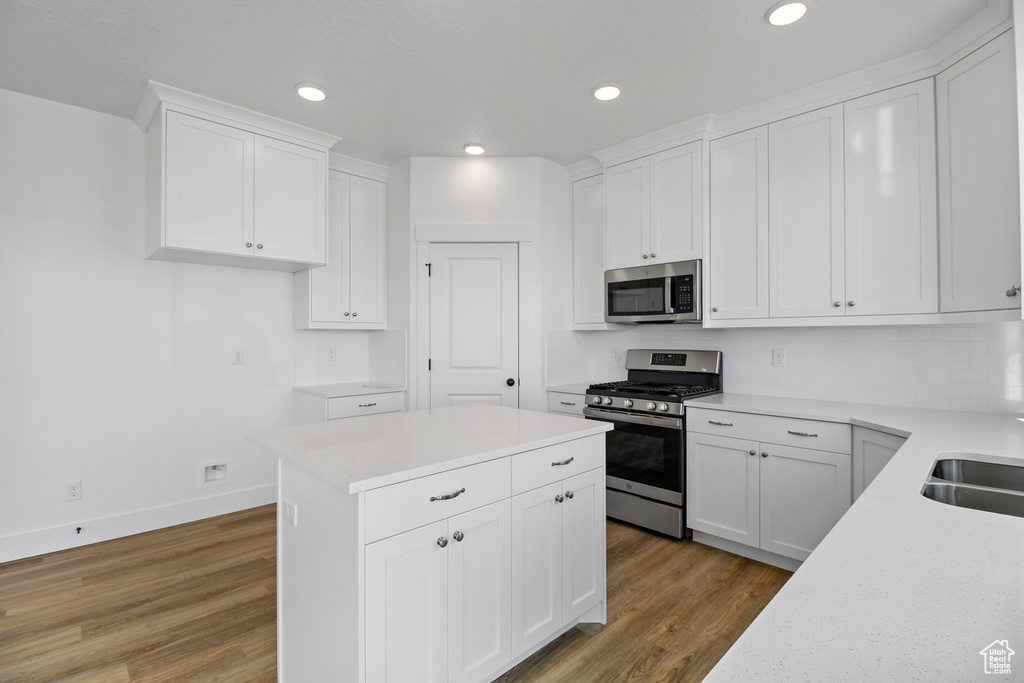 Kitchen featuring stainless steel appliances, wood finished floors, backsplash, white cabinets, and light countertops