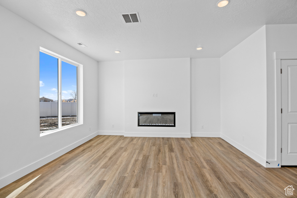 Unfurnished living room with light wood finished floors, recessed lighting, a glass covered fireplace, and a textured ceiling