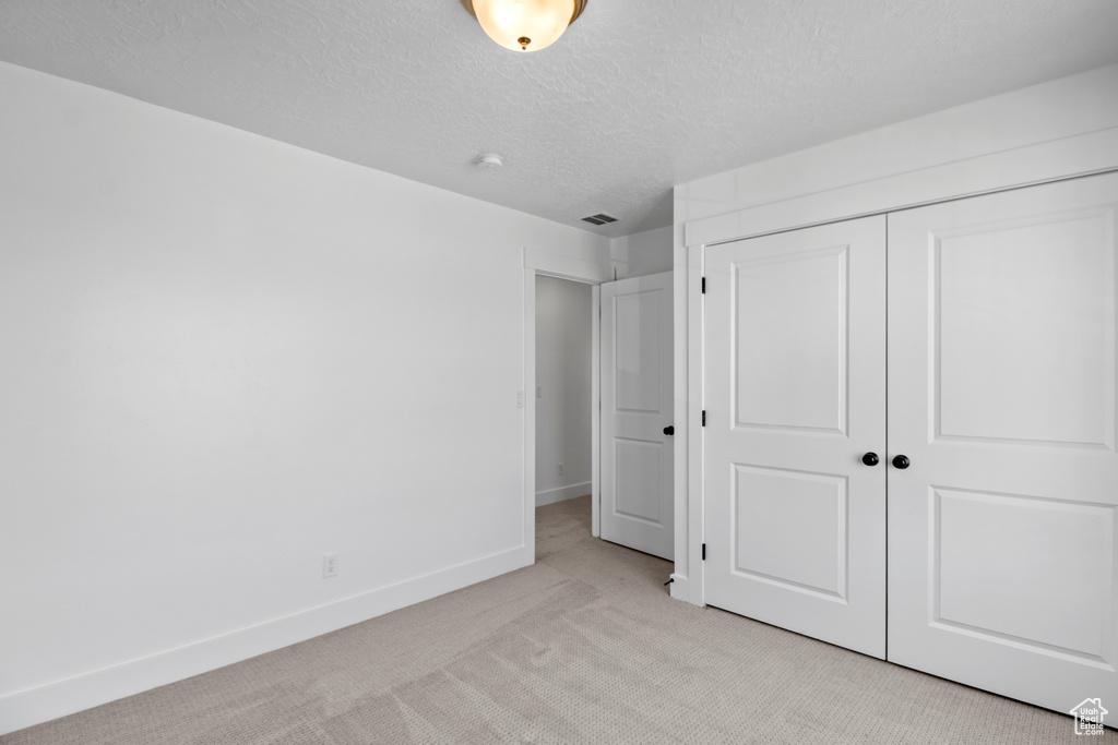 Unfurnished bedroom featuring light carpet, a closet, and a textured ceiling