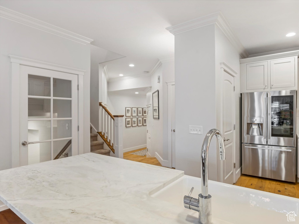 Kitchen with stainless steel fridge with ice dispenser, ornamental molding, light stone countertops, recessed lighting, and a sink