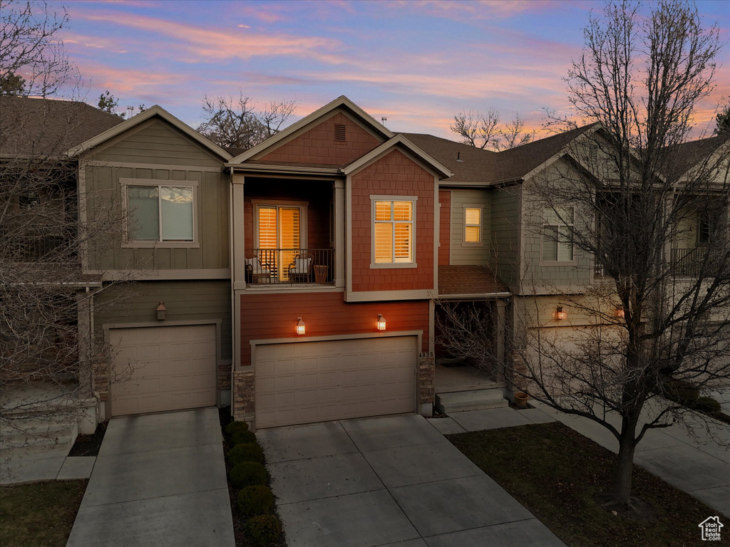 View of front of home featuring an attached garage, driveway, stone siding, board and batten siding, and a balcony