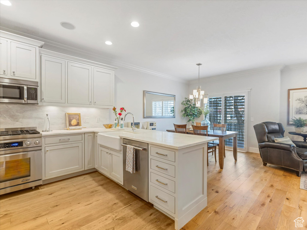 Kitchen with appliances with stainless steel finishes, a sink, a peninsula, light countertops, and ornamental molding