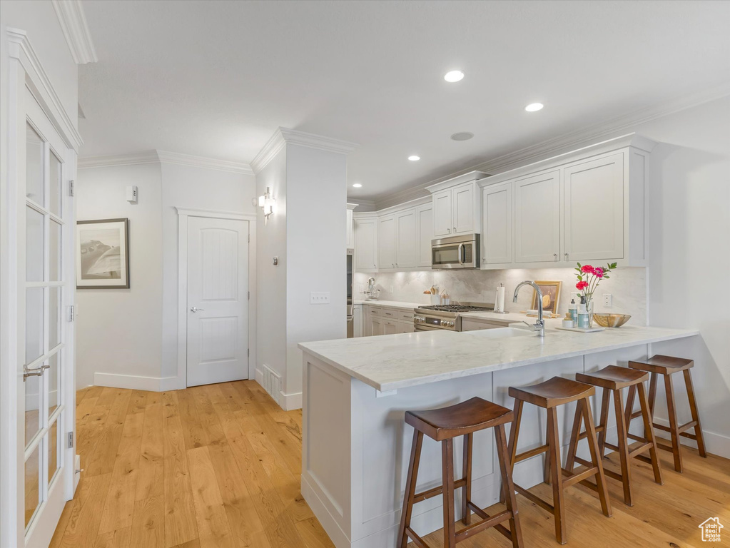 Kitchen featuring appliances with stainless steel finishes, decorative backsplash, a peninsula, light wood finished floors, and ornamental molding