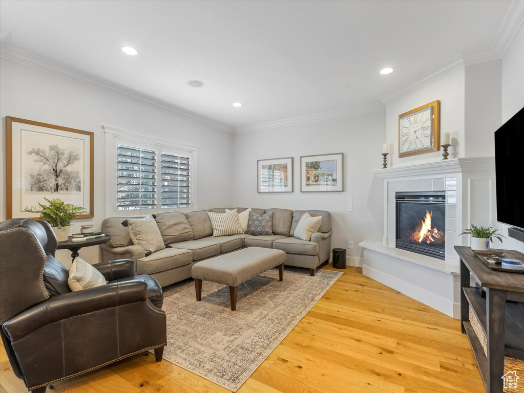 Living room featuring ornamental molding, light wood finished floors, recessed lighting, a fireplace, and baseboards
