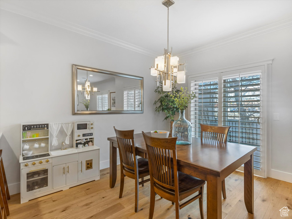 Dining space with a chandelier, crown molding, healthy amount of natural light, and light wood-type flooring