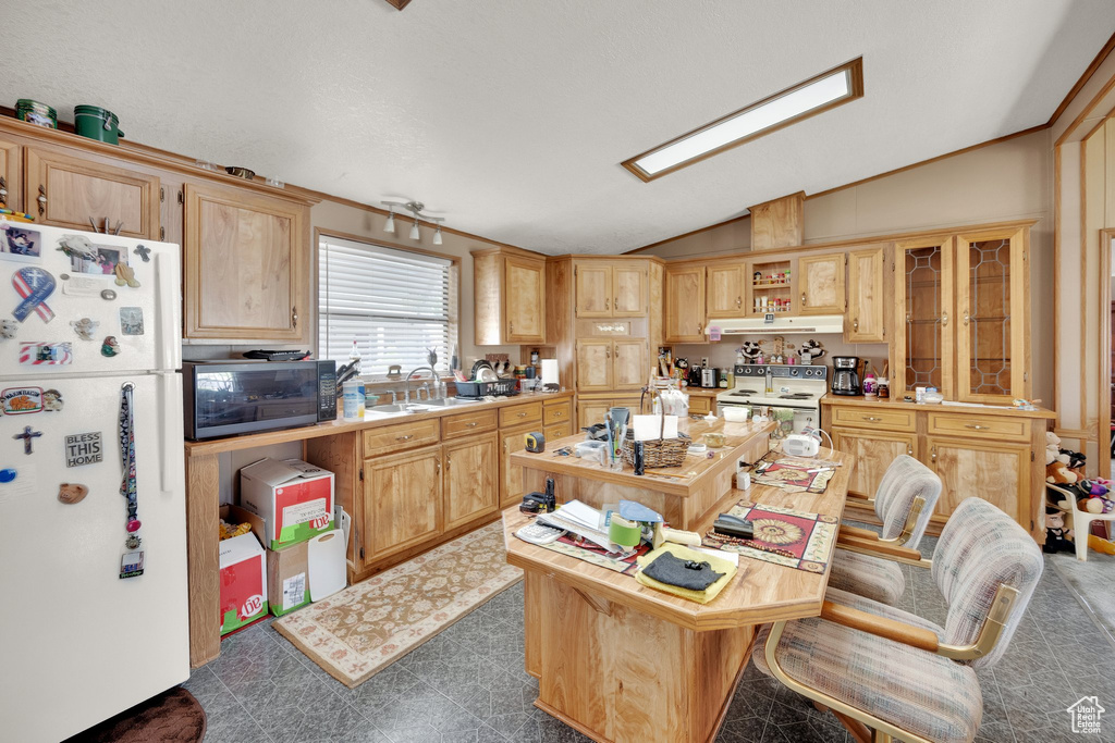 Kitchen with white appliances, lofted ceiling, under cabinet range hood, light countertops, and light brown cabinetry