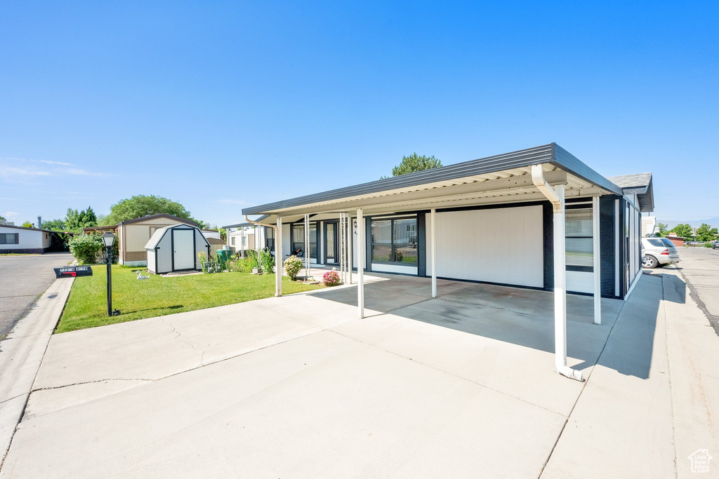 View of front of house featuring a storage shed, a front yard, concrete driveway, and an attached carport