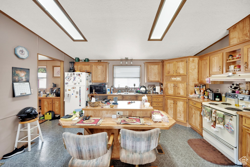 Kitchen with white appliances, vaulted ceiling, under cabinet range hood, and light countertops