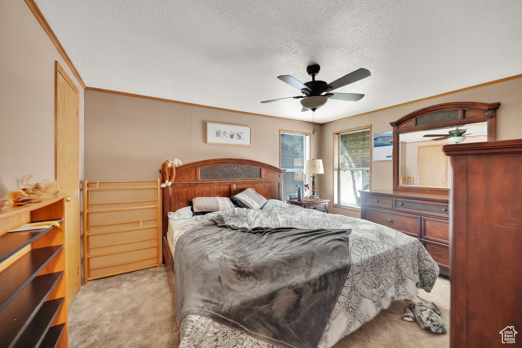 Bedroom with light colored carpet, a textured ceiling, ornamental molding, and ceiling fan