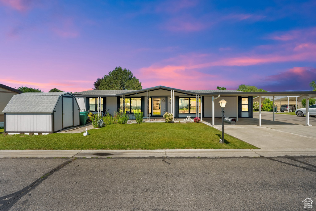 View of front of house featuring a storage shed, a lawn, concrete driveway, and a carport
