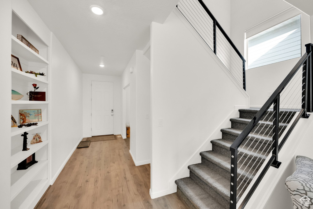 Hall with stairway, light wood-type flooring, recessed lighting, and built in shelves