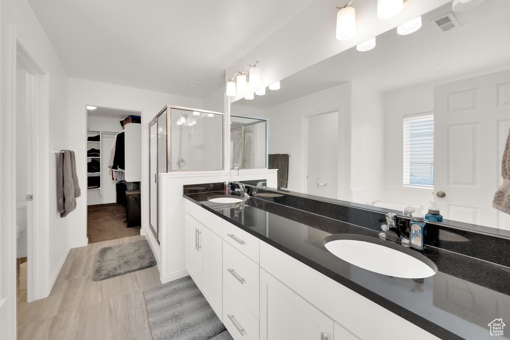 Full bath with a shower stall, double vanity, and a spacious closet