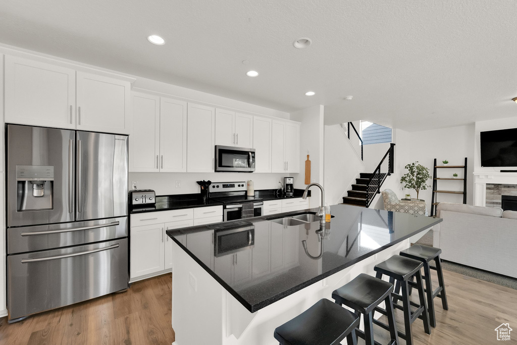 Kitchen featuring stainless steel appliances, open floor plan, white cabinetry, a kitchen bar, and recessed lighting