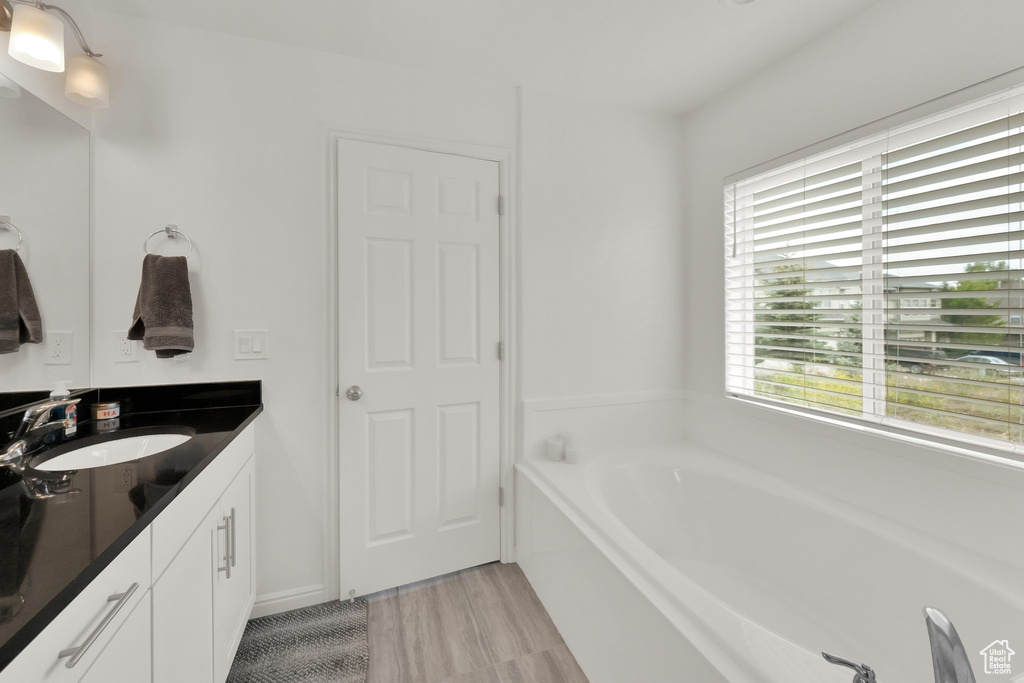 Full bath with vanity, a bath, and wood finished floors