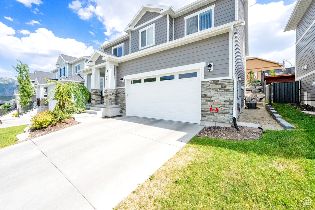 Craftsman-style home with stone siding, an attached garage, driveway, a residential view, and a front yard