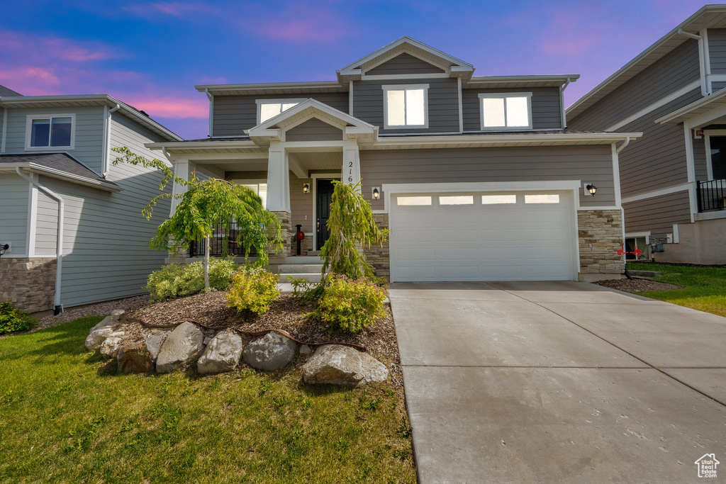 View of front of home featuring driveway, a garage, stone siding, a porch, and a front lawn