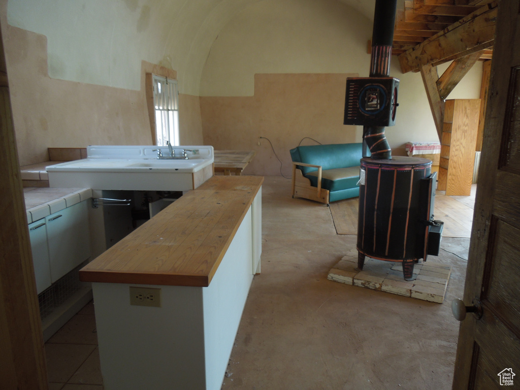 Kitchen with wooden counters, vaulted ceiling, concrete flooring, a wood stove, and white cabinets